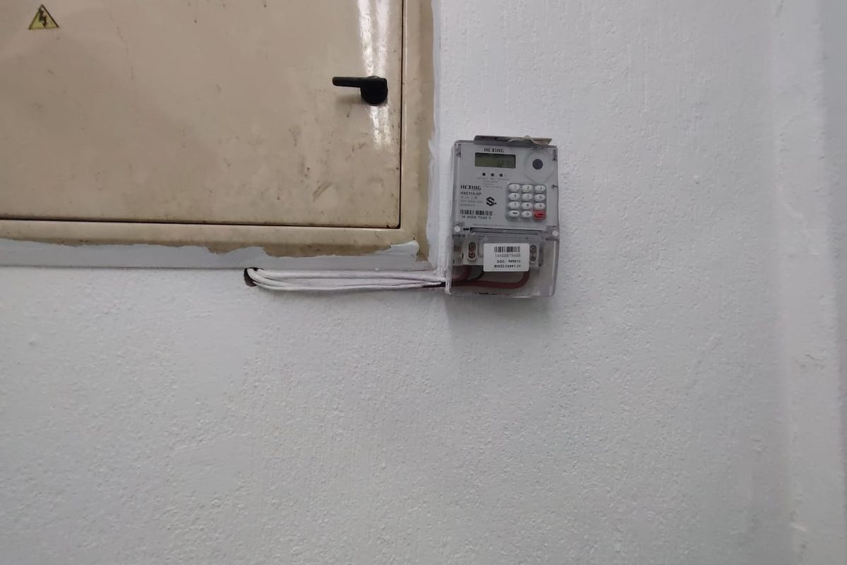 A utility wall featuring a mounted electrical distribution board and a prepaid electricity meter.