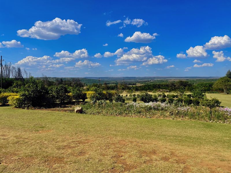 A scenic view of the expansive landscaped garden and surrounding rural landscape under a clear blue sky.