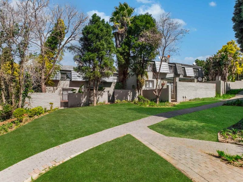 Front view of the apartment complex featuring a well-maintained lawn, paved walkways, and established garden landscaping.