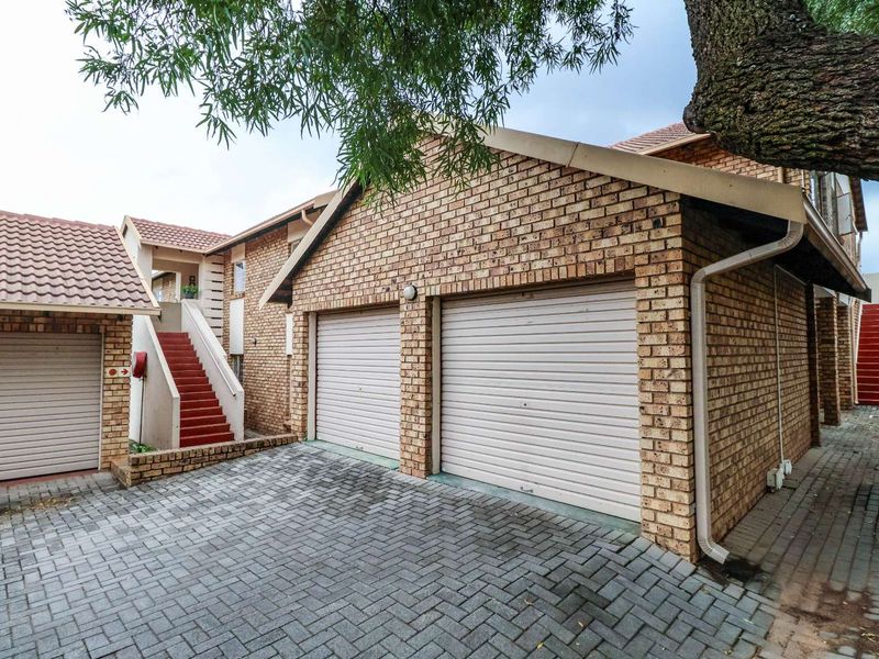 Exterior view of a brick apartment complex featuring a double garage, paved driveway, and an external staircase leading to upper levels.