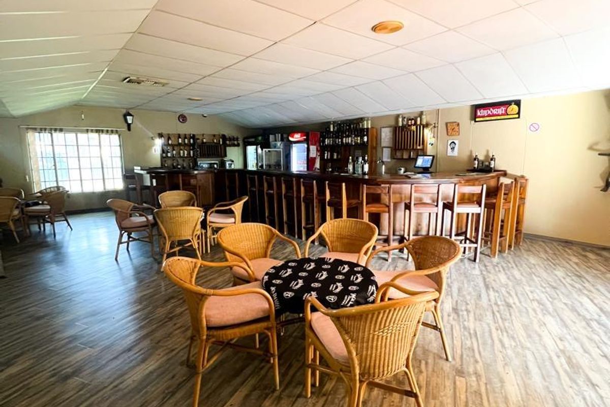 A spacious hotel bar area featuring a long built-in service counter, wood-look flooring, and a suspended ceiling.