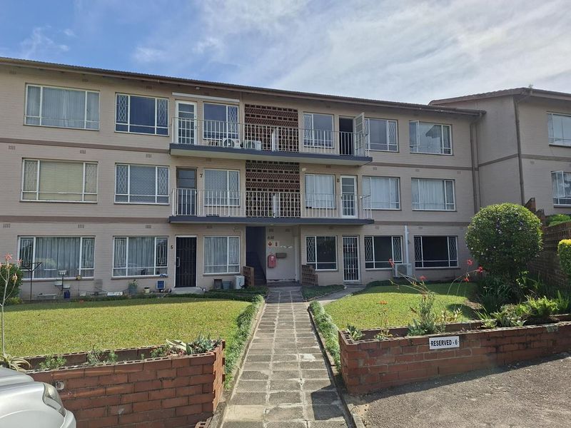 Front elevation of a multi-story apartment complex featuring brick facade, private balconies, and a landscaped entrance walkway.