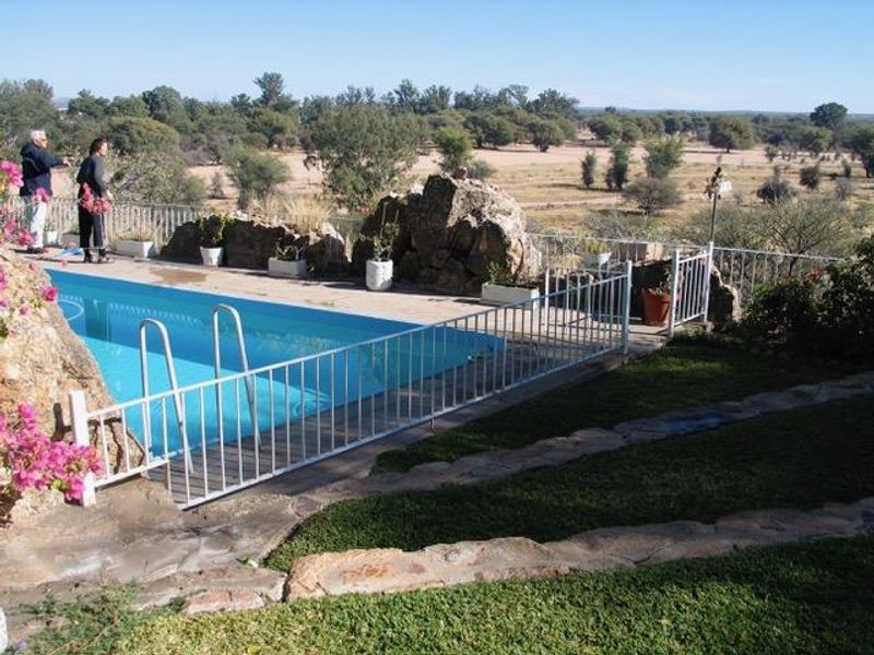 Outdoor swimming pool area featuring metal safety fencing, natural rock features, and stone paving overlooking a scenic landscape.
