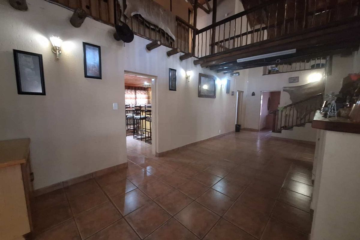 Spacious living area featuring tiled flooring, exposed timber beams, and a mezzanine level with a wooden balcony railing.