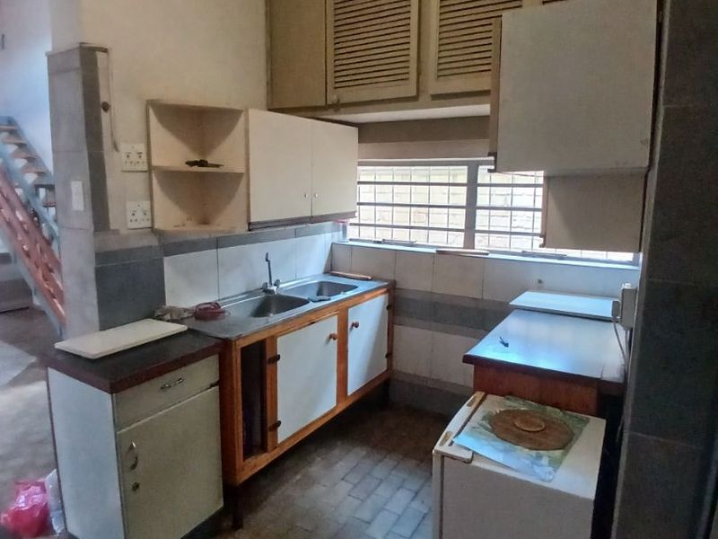 A dated kitchen featuring original built-in cabinetry, a double basin sink, and tiled backsplash, offering significant potential for a modern renovation.