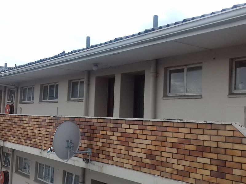Exterior view of an apartment building facade featuring a brick balcony, tiled roof, and multiple window units.