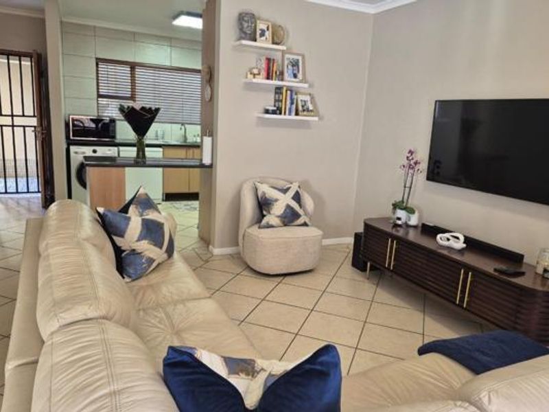 Open-plan living area featuring tiled flooring and a connected kitchen space with built-in cabinetry and a breakfast bar.