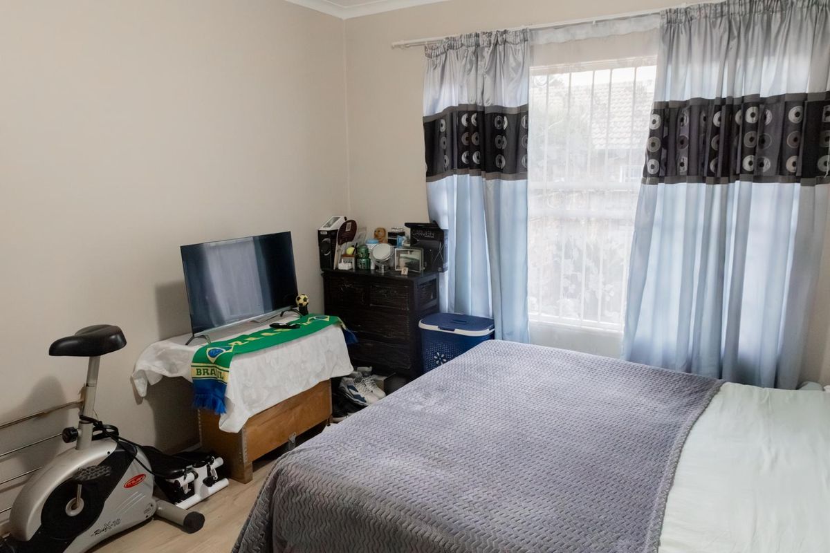 A standard bedroom featuring light-toned flooring, a window with security bars, and neutral wall finishes.