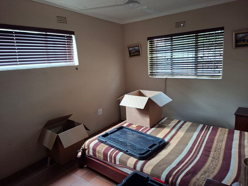 A bedroom featuring tiled flooring, a ceiling fan, and venetian blinds on the windows.