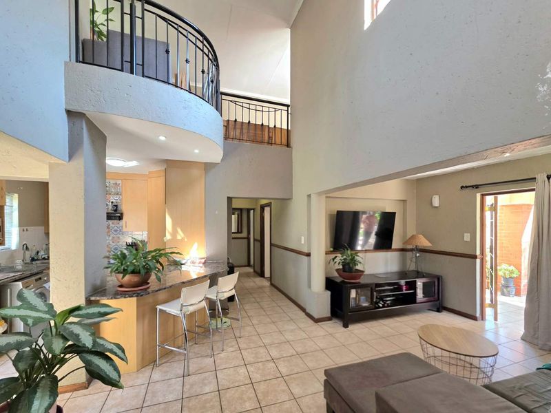 Spacious open-plan living area featuring a double-volume ceiling, granite breakfast bar, and a mezzanine level with wrought iron railings.