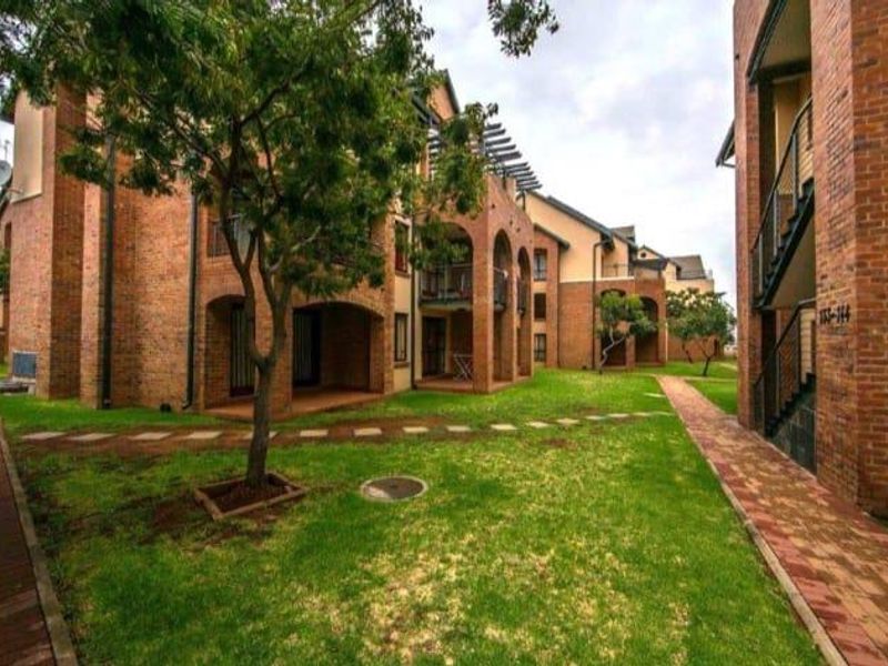Exterior view of a face brick apartment complex featuring landscaped lawns, paved walkways, and covered patio areas.