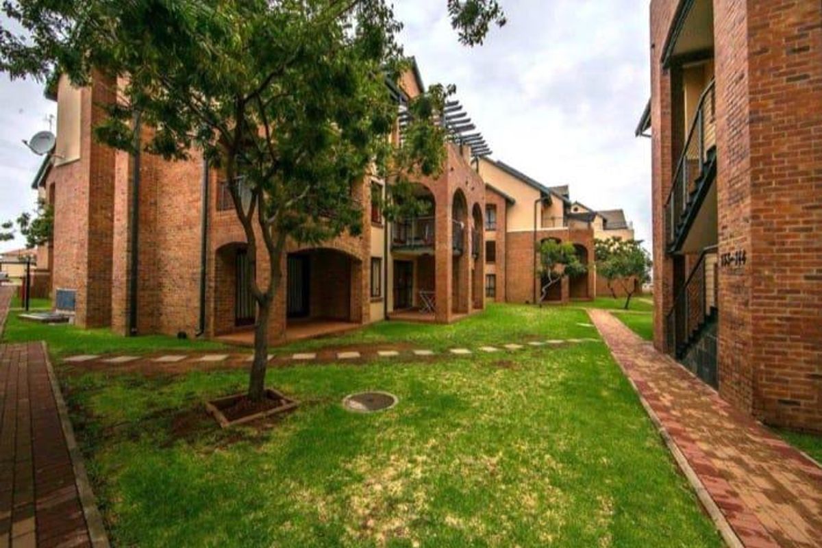 Exterior view of a face brick apartment complex featuring landscaped lawns, paved walkways, and covered patio areas.