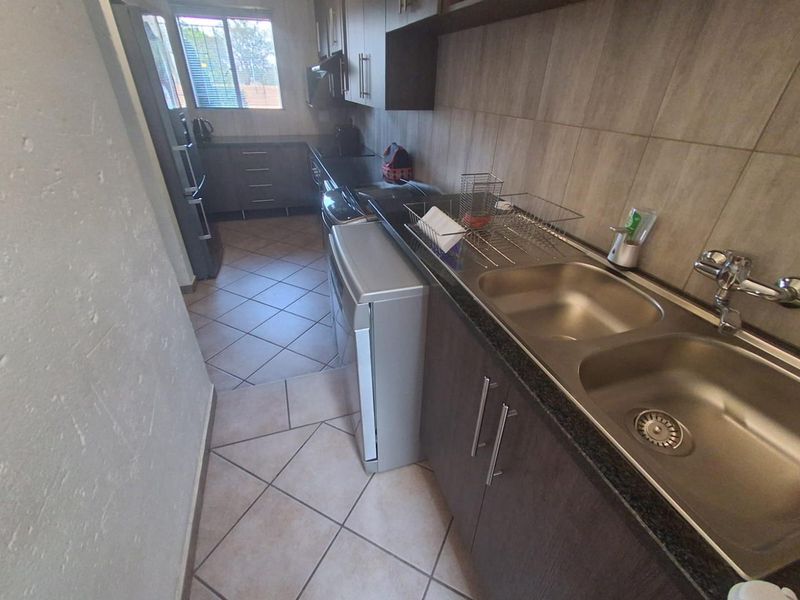 A functional kitchen featuring dark wood-look cabinetry, granite countertops, a double stainless steel sink, and neutral ceramic floor tiles.