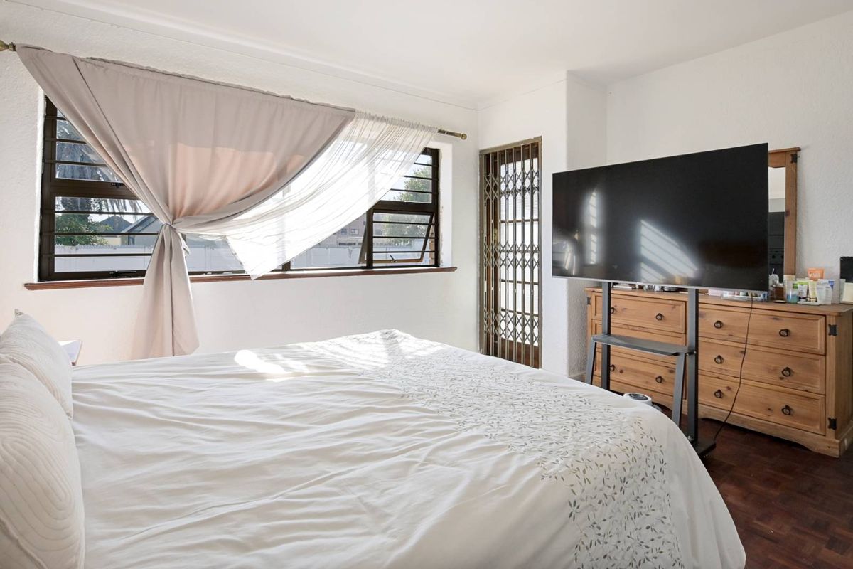 A bright bedroom featuring dark wood flooring, a large window with natural light, and a security gate leading to an outdoor area.