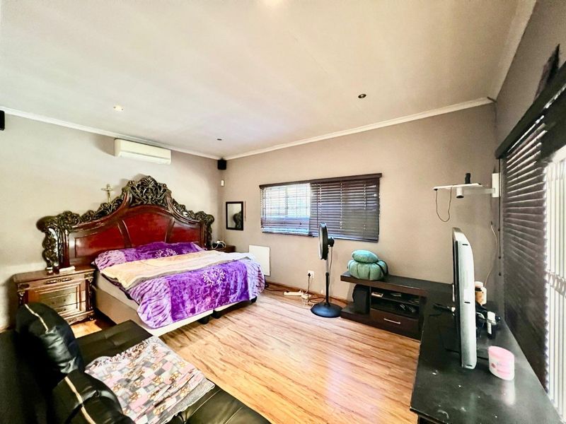 Spacious bedroom featuring laminate flooring, recessed lighting, and a wall-mounted air conditioning unit, offering a comfortable and functional living space.