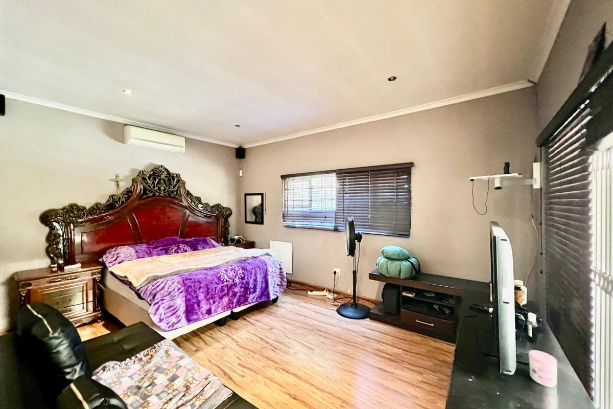 Spacious bedroom featuring laminate flooring, recessed lighting, and a wall-mounted air conditioning unit, offering a comfortable and functional living space.