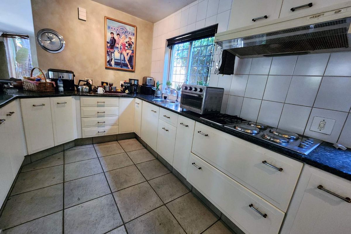 A functional kitchen featuring white cabinetry, dark countertops, a gas hob with extractor fan, and tiled flooring throughout.