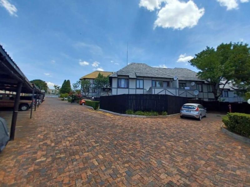 Exterior view of the apartment complex featuring a paved driveway, covered parking bays, and traditional timber-accented building facades.