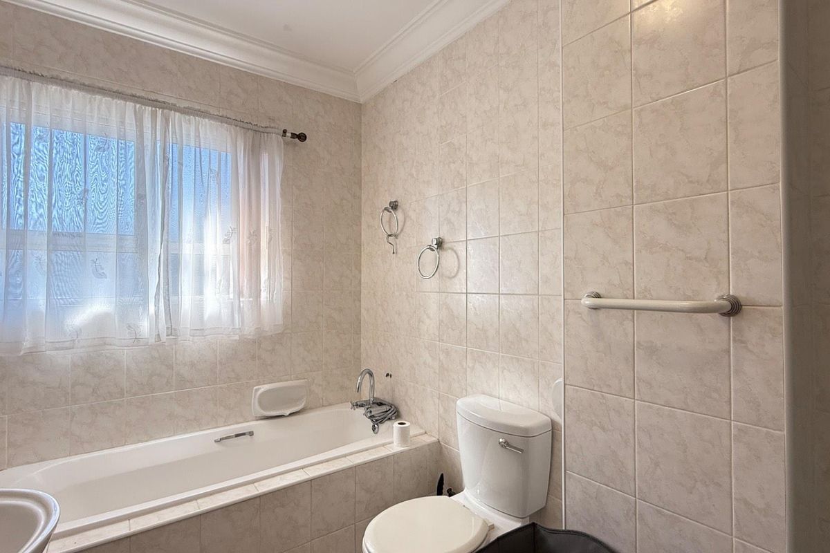 A functional bathroom featuring a built-in bathtub, a standard toilet, and neutral wall tiling throughout.