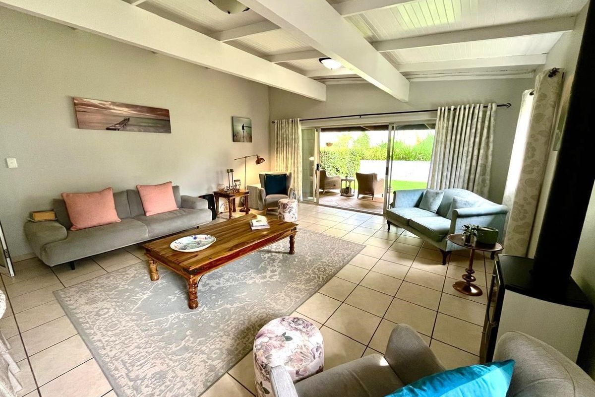 Spacious living room featuring exposed beam ceilings, tiled flooring, and large sliding glass doors providing seamless access to the outdoor patio and garden area.