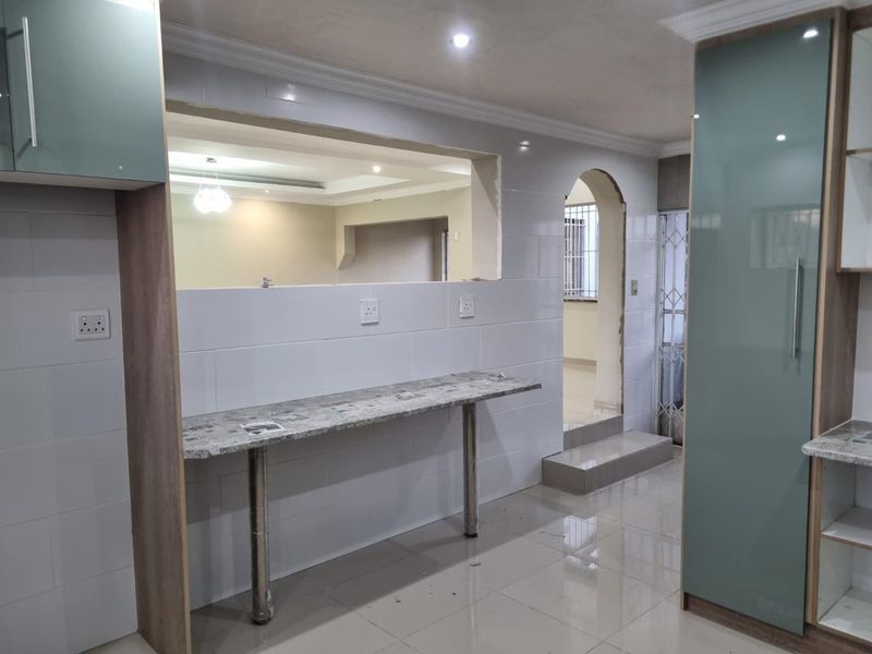A modern kitchen area featuring a granite breakfast bar, tiled splashbacks, and built-in cabinetry, with an open-plan layout connecting to adjacent living spaces.