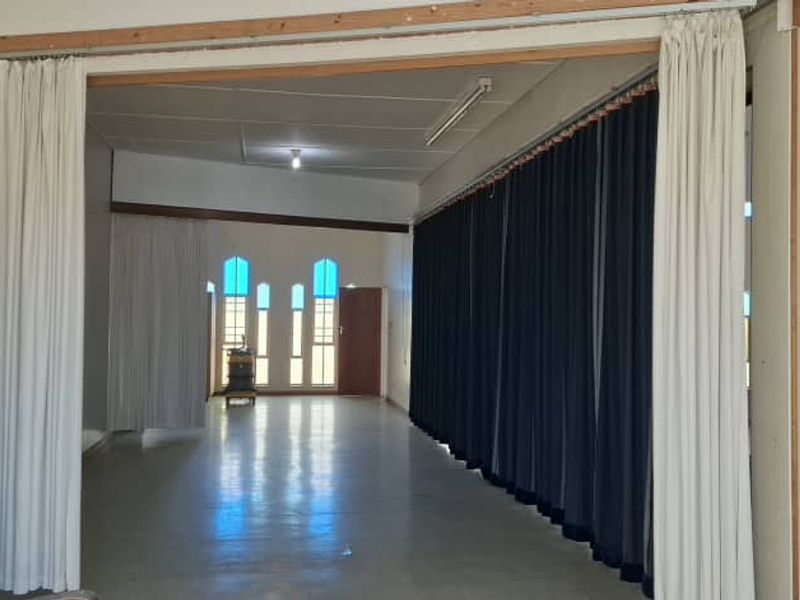A large, open-plan interior space featuring sliding room dividers, arched windows, and functional lighting, suitable for versatile use in a mixed-use property.