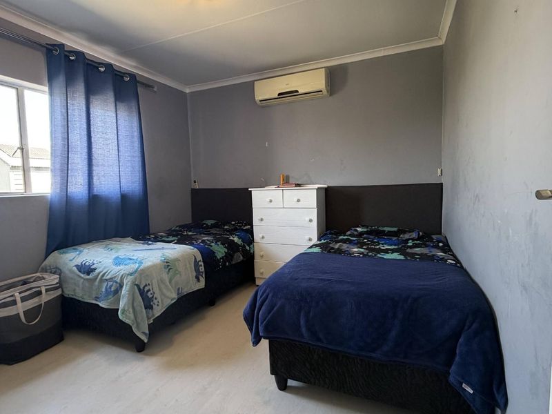 A functional bedroom featuring laminate flooring, coving, and a wall-mounted air conditioning unit.