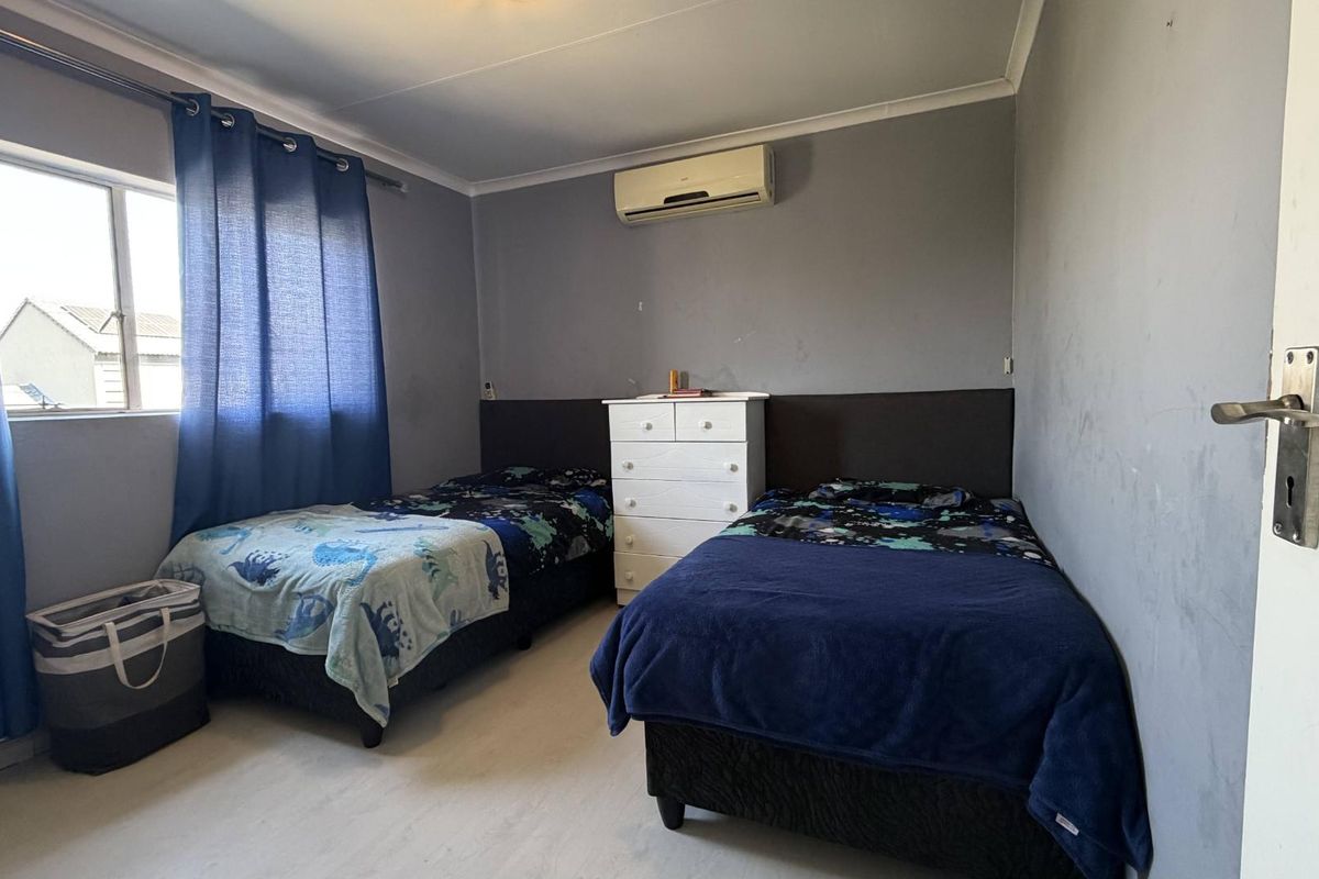 A functional bedroom featuring laminate flooring, coving, and a wall-mounted air conditioning unit.
