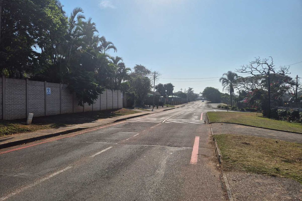 A view of the street showing the asphalt road, paved verge, and a precast concrete boundary wall along the property perimeter.