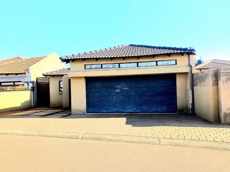 Front view of the property featuring a paved driveway, a single garage with a blue door, and a tiled roof.