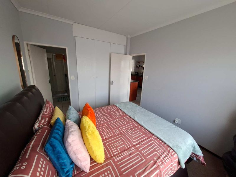 A bedroom featuring built-in cupboards and neutral wall finishes, with direct access to an adjacent bathroom and kitchen area.