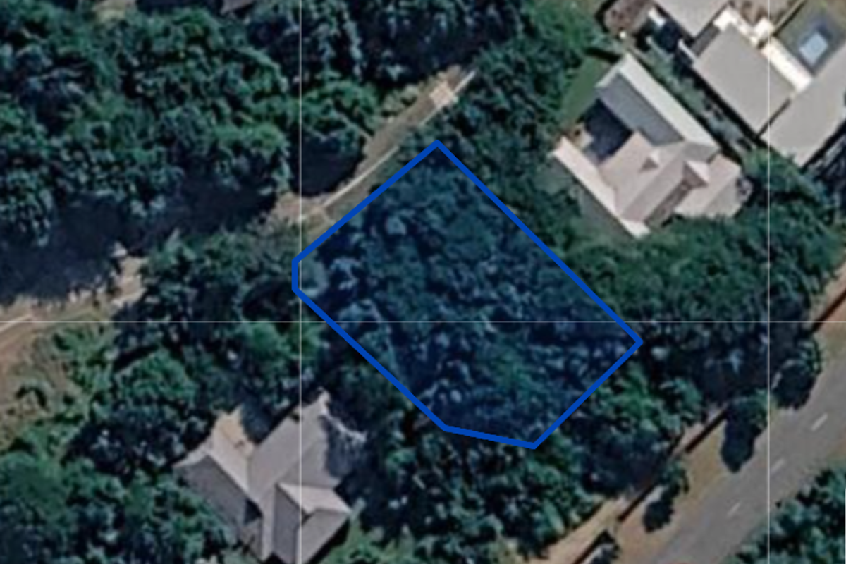 An aerial view of a vacant residential plot highlighted with a blue boundary outline, surrounded by established trees and neighboring properties.