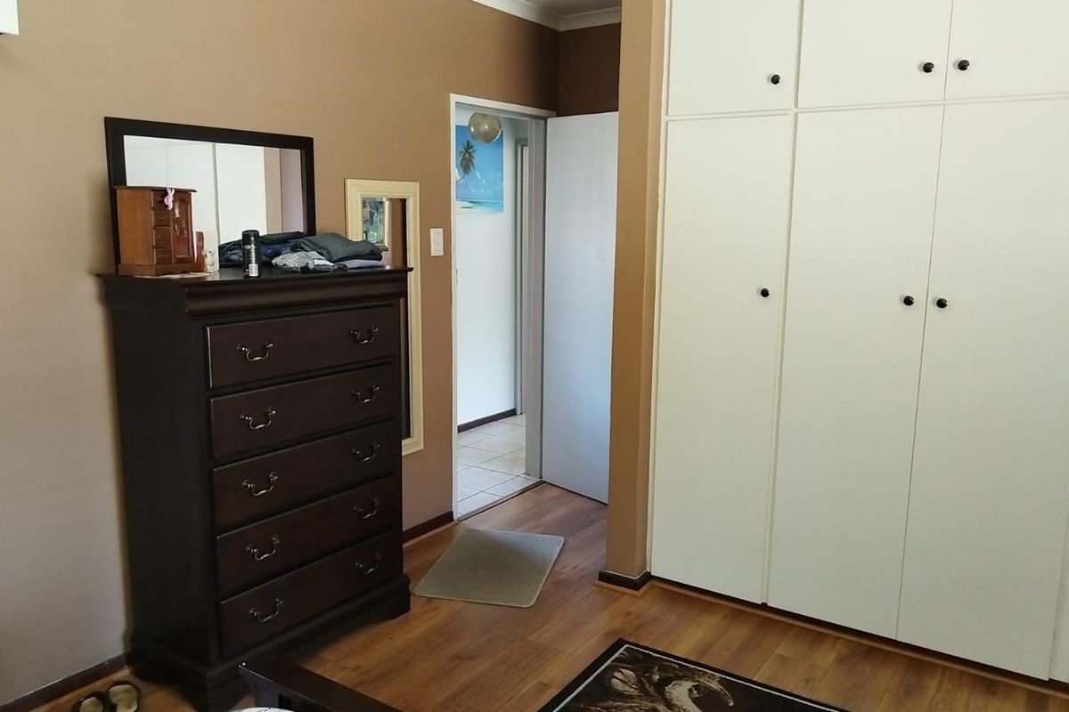 A bedroom featuring built-in floor-to-ceiling wardrobes, laminate wood flooring, and neutral wall tones, providing functional storage and access to an adjoining hallway.