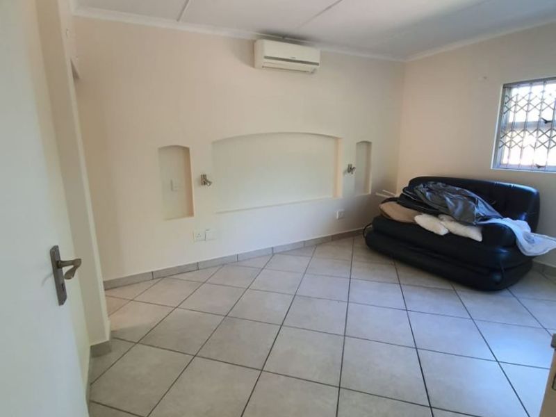A spacious bedroom featuring tiled flooring, a wall-mounted air conditioning unit, and decorative recessed wall niches with integrated lighting.