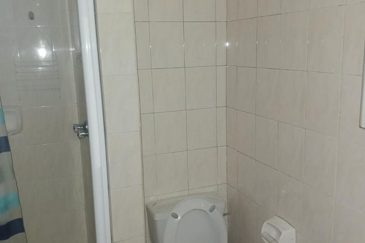 A functional bathroom featuring a shower enclosure with a glass door, a standard toilet, and neutral wall tiling.