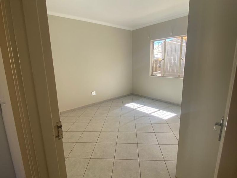 A clean, empty bedroom featuring neutral wall paint, ceramic floor tiles, and a window fitted with security bars.