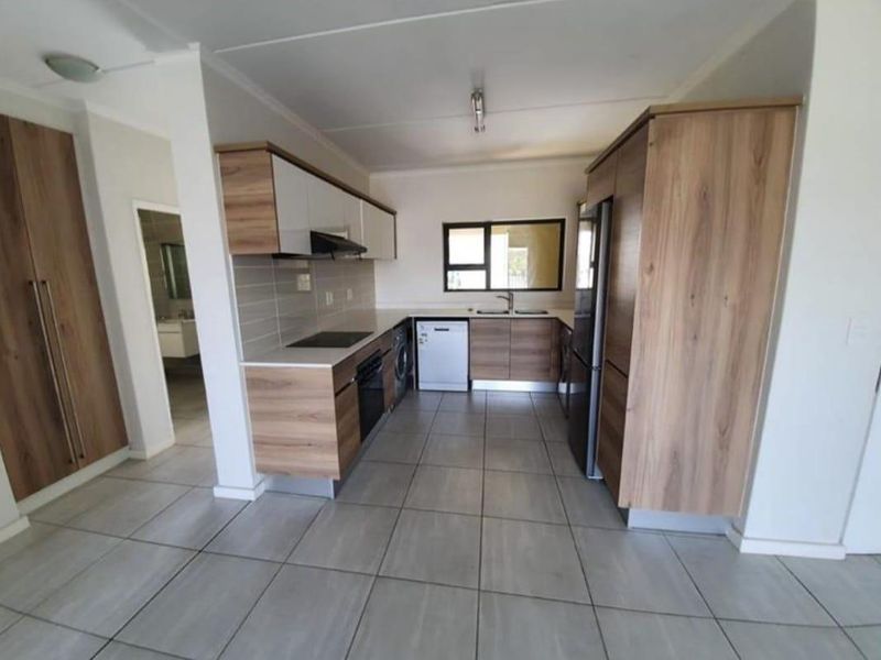 Modern kitchen featuring wood-finish cabinetry, tiled flooring, integrated appliances, and a functional layout with ample storage and workspace.