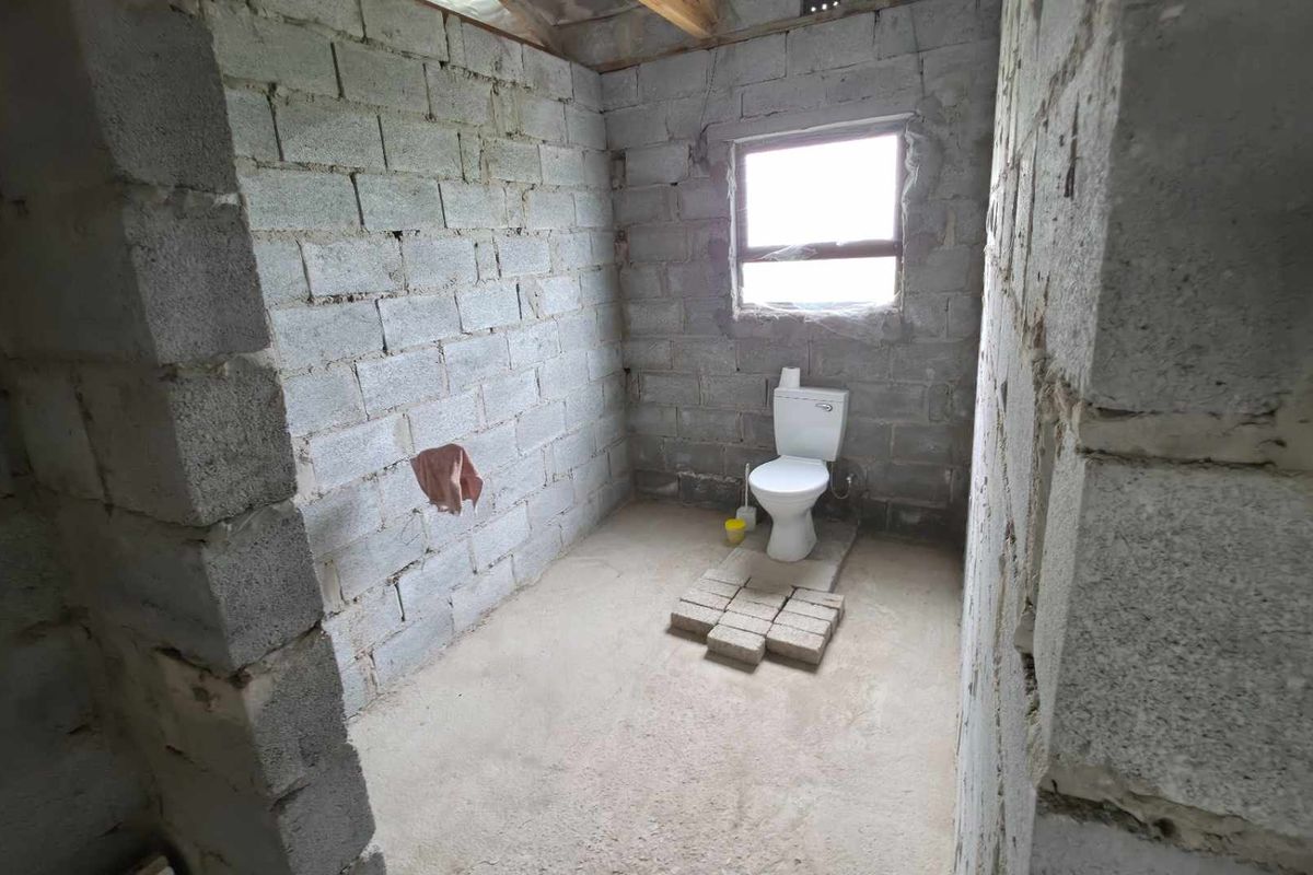 An unfinished bathroom space featuring exposed concrete block walls, a concrete floor, and a single installed toilet.