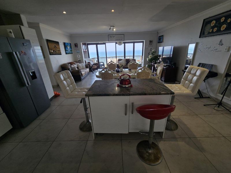 Spacious open-plan living and kitchen area featuring tiled floors, a granite-topped island, and large sliding doors offering expansive ocean views.