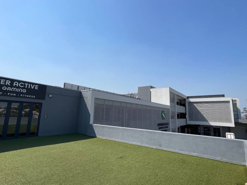 A modern commercial building exterior featuring a rooftop terrace with artificial turf, louvred screens, and large folding glass doors for access.