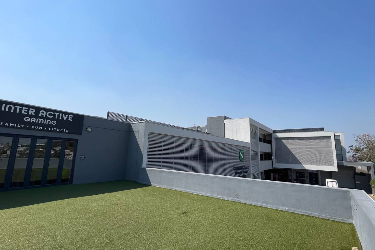 A modern commercial building exterior featuring a rooftop terrace with artificial turf, louvred screens, and large folding glass doors for access.