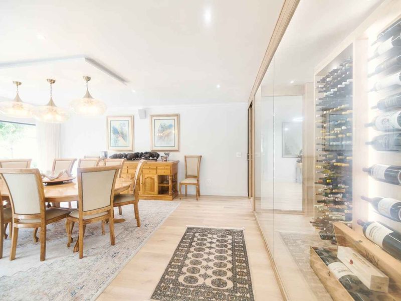 Elegant dining area featuring light hardwood flooring, recessed lighting, and a sophisticated glass-enclosed built-in wine cellar display.