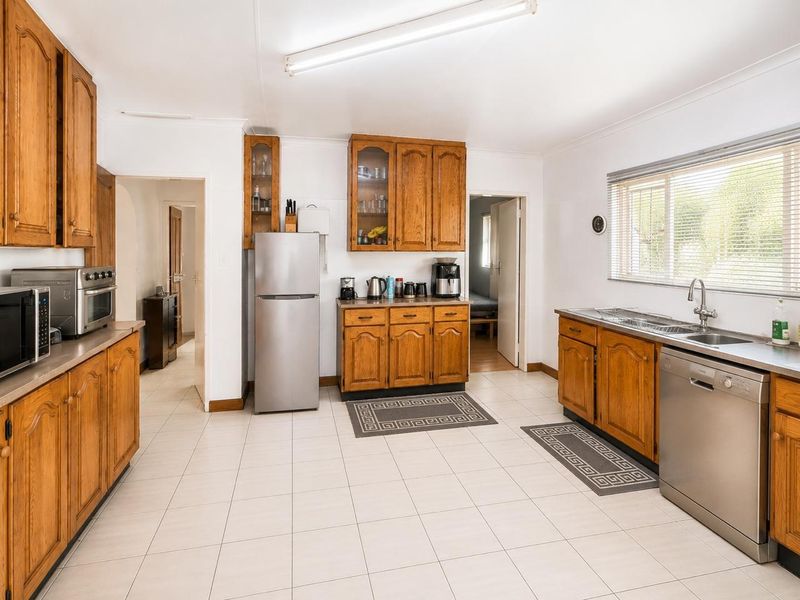 A functional kitchen featuring traditional wooden cabinetry, tiled flooring, and stainless steel sink, offering a clean and practical workspace.