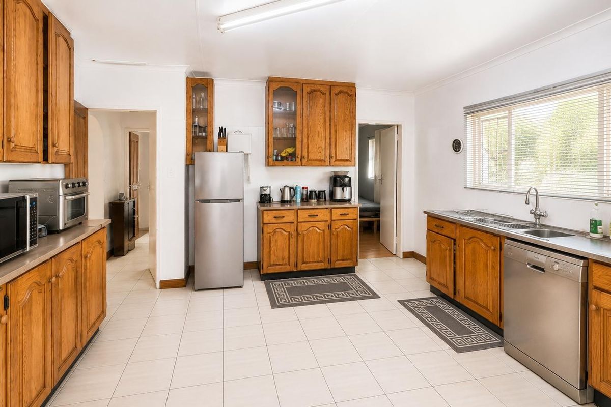 A functional kitchen featuring traditional wooden cabinetry, tiled flooring, and stainless steel sink, offering a clean and practical workspace.