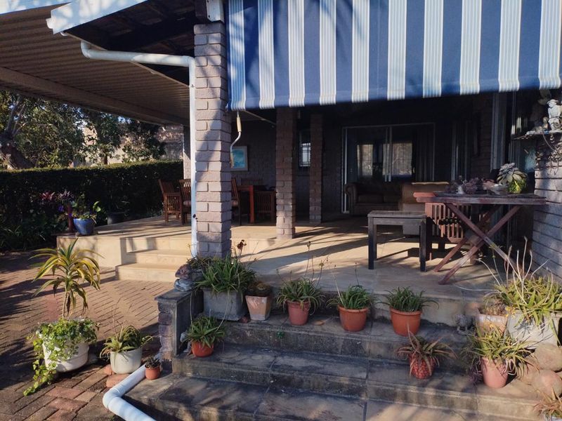 A covered outdoor patio area featuring brick pillars, paved flooring, and a retractable striped awning, providing a functional space for outdoor living.