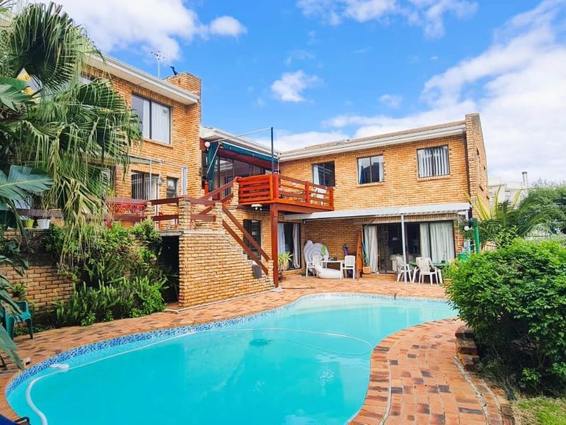 A spacious outdoor pool area featuring a swimming pool, brick-paved surround, and a raised wooden deck attached to the two-story brick apartment building.
