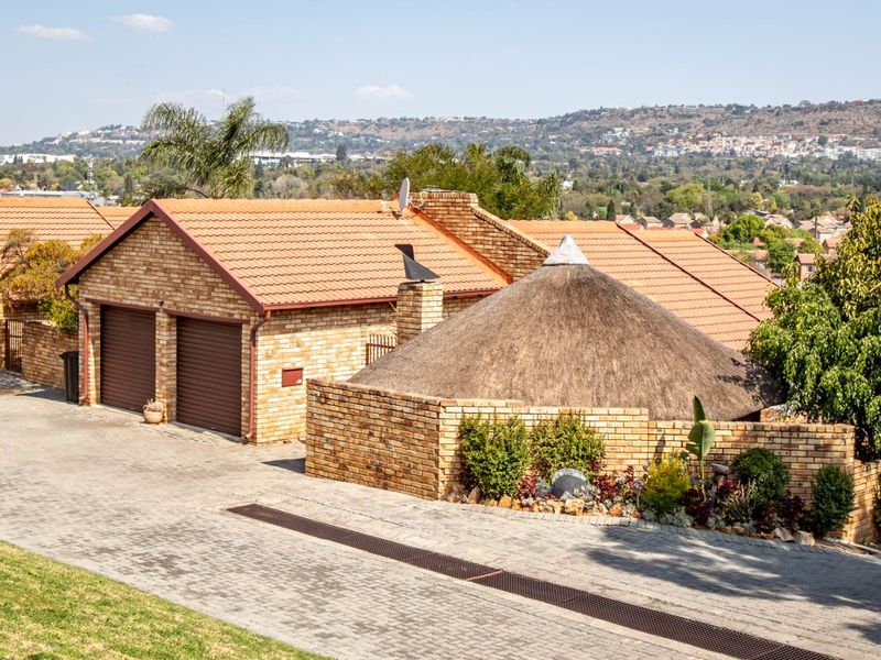 Front exterior view of a townhouse featuring a double garage, brick construction, and a distinctive thatched roof section with a paved driveway.