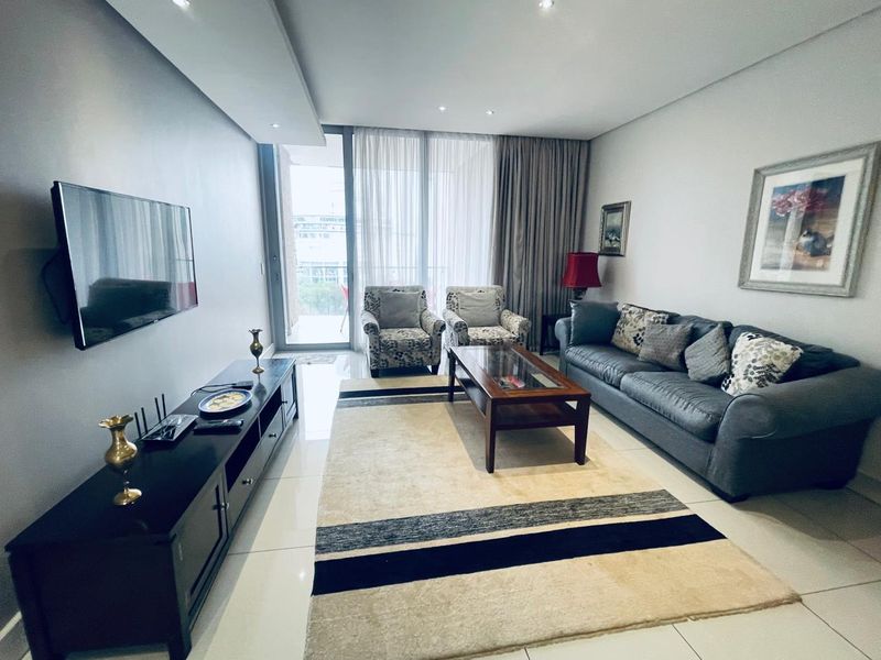A well-maintained living room featuring tiled flooring, recessed ceiling lights, and a large sliding glass door providing access to the balcony.