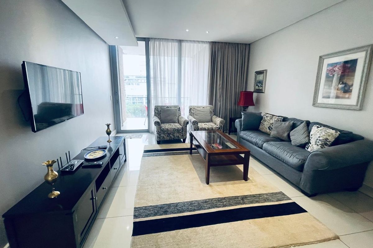A well-maintained living room featuring tiled flooring, recessed ceiling lights, and a large sliding glass door providing access to the balcony.