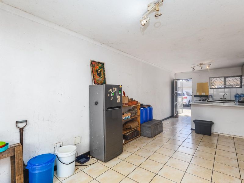 Open-plan kitchen and living area featuring ceramic floor tiles, basic cabinetry, and direct access to the exterior via a security gate.